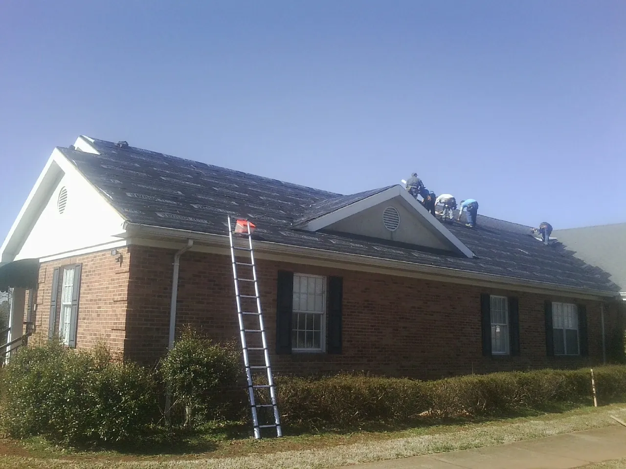 Crew tearing shingles off a brick ranch roof with a ladder set — Metal Roof Repair work by our crew in Medford
