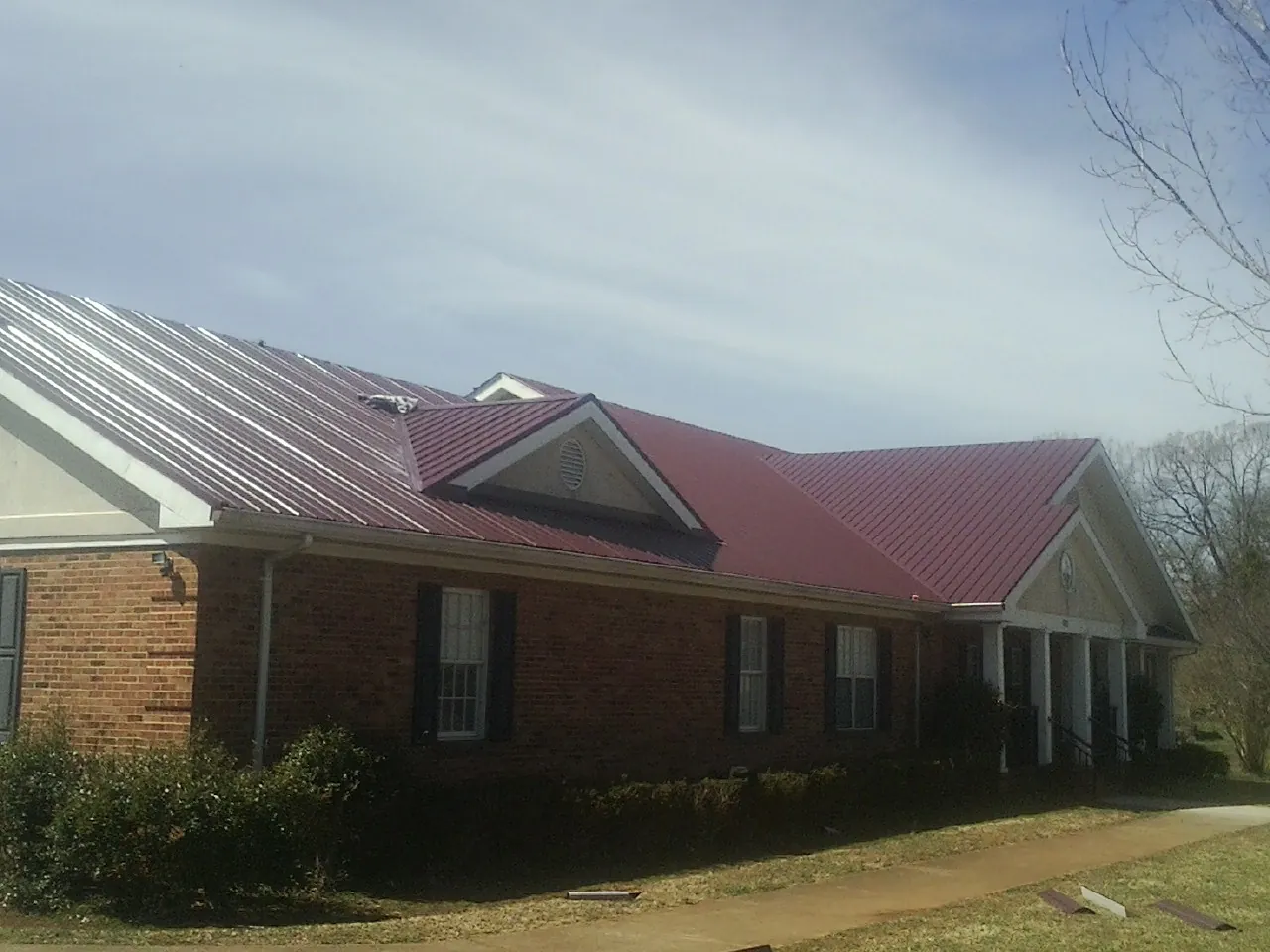 Red metal roof with gabled entries on a long brick building, from a Hail Damage Roof Repair job in Medford